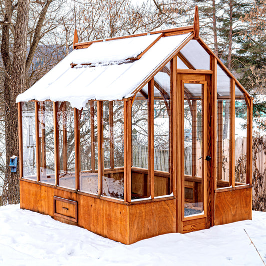 Exterior of Trillium model in snow with redwood framing, glass walls, and polycarbonate roof