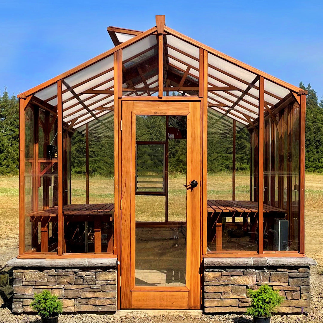 Wooden Artisan greenhouse with stone foundation in a field with trees in the background