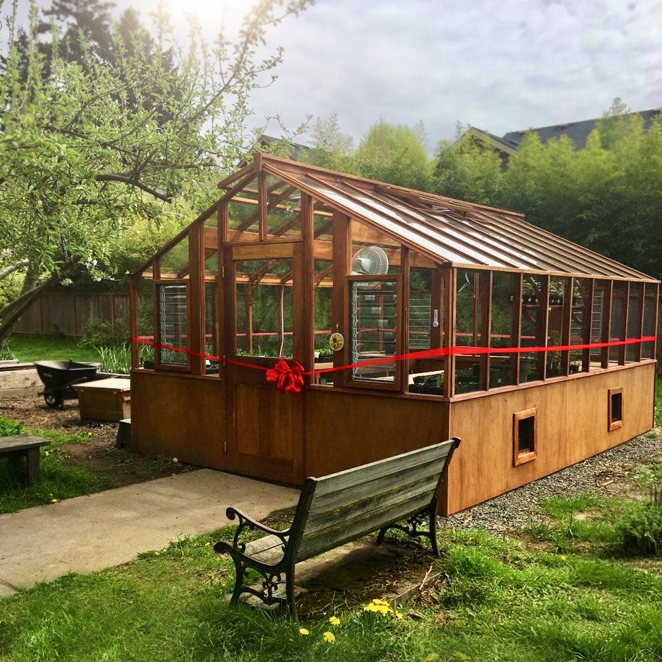 Wooden Heirloom greenhouse with a red ribbon in a garden setting