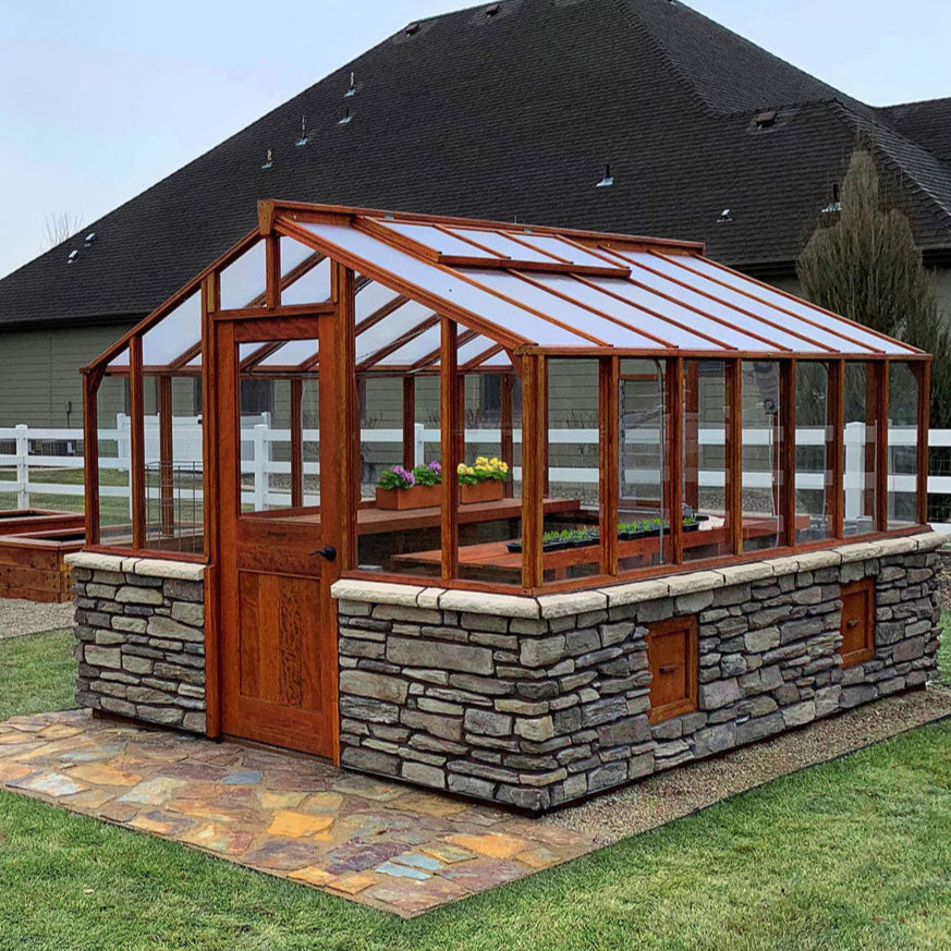 Wooden greenhouse with stone foundation on a grassy lawn