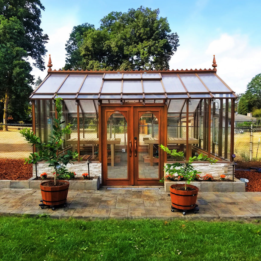 Glass Nantucket greenhouse with wooden doors in a garden setting