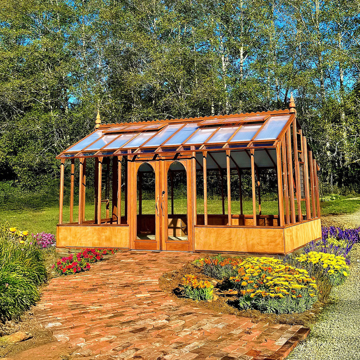Wooden Nantucket greenhouse with glass panels in a garden setting with flowers and trees.