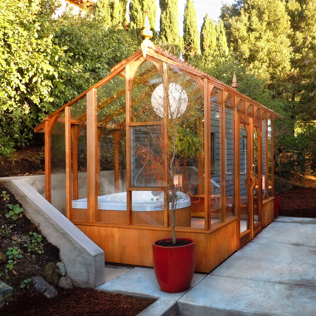 Wooden Nantucket greenhouse with hot tub spa and glass walls in a backyard garden setting