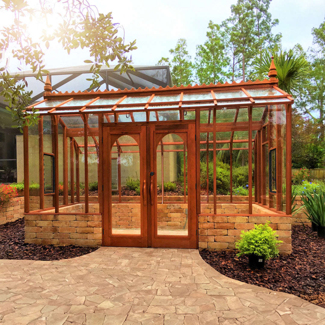 Wooden Nantucket greenhouse with glass panels in a garden setting with stone base wall