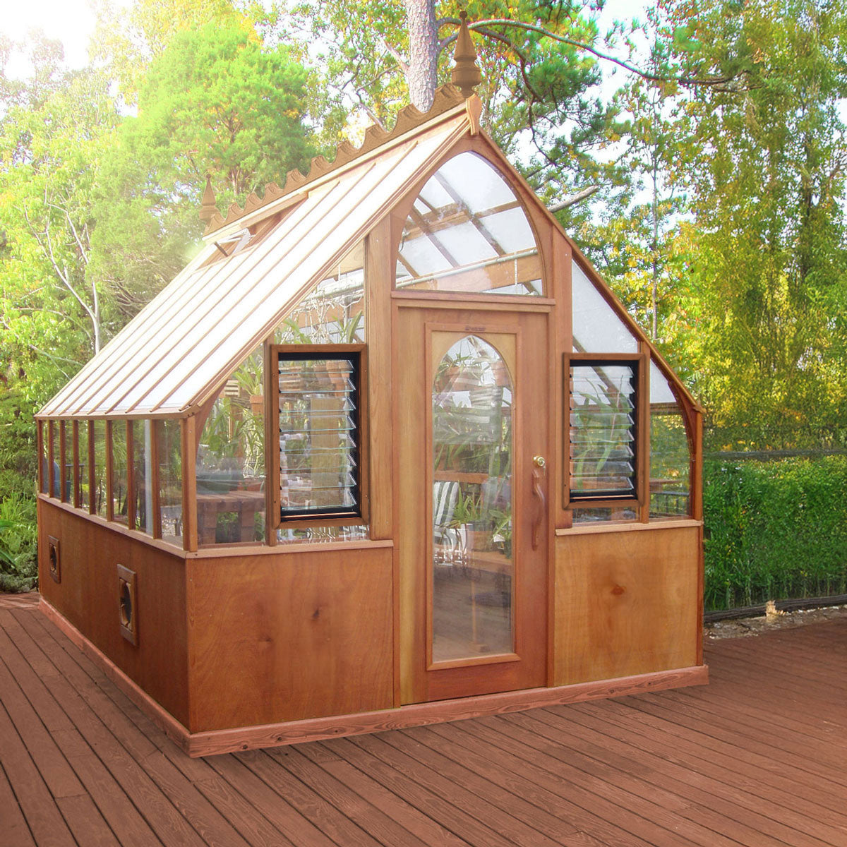 Wooden greenhouse with glass panels on a wooden deck surrounded by trees
