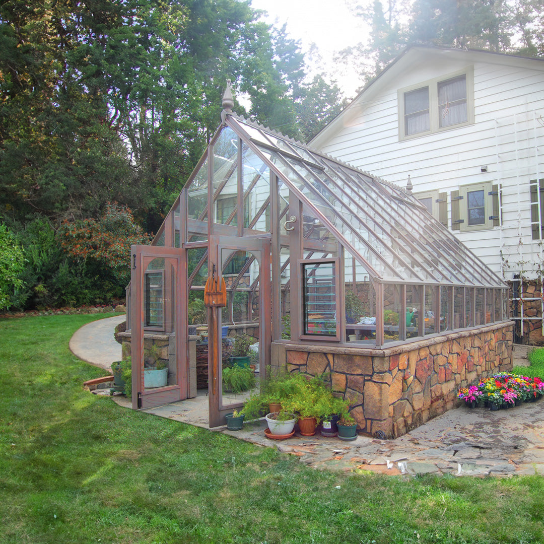 Tudor Greenhouse with double doors and stone foundation, surrounded by garden and trees.