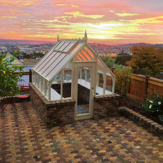 Tudor Greenhouse with arched entry doors at sunset, showing redwood frame and masonry base.