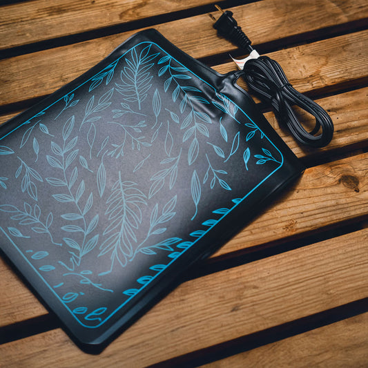 Black seed starting heat mat with leaf pattern on a wooden surface