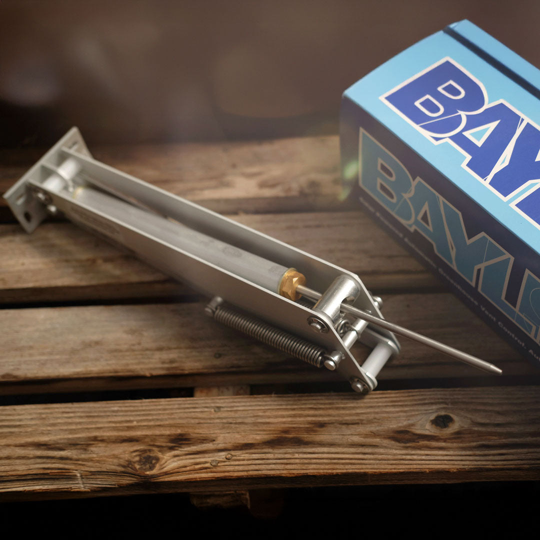 Metal spring-loaded device on a wooden surface with a blue box labeled 'BAXI' in the background.