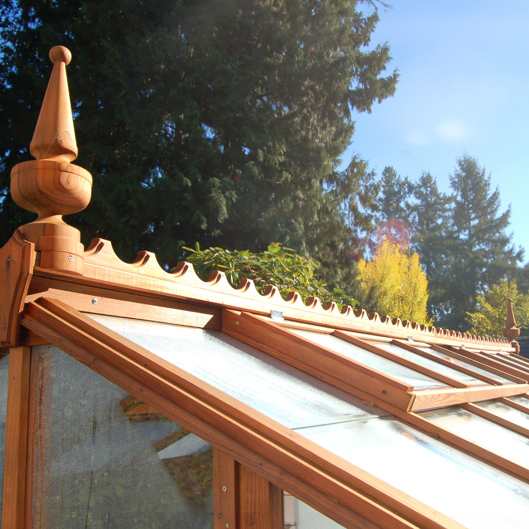 Wooden roof structure with glass panels and decorative finials and ridge scalloping against a tree-filled background