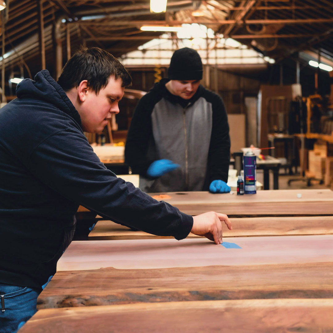 Two people working on wooden planks in a workshop setting.