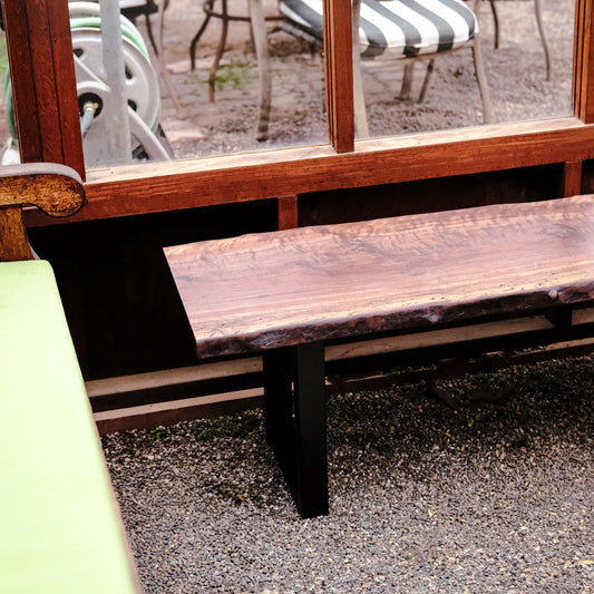 Wooden bench with a black base on a gravel surface, with a blurred outdoor background.