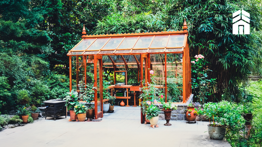 Luxury redwood greenhouse by Sturdi Built surrounded by plants, featuring clear glass and premium craftsmanship.