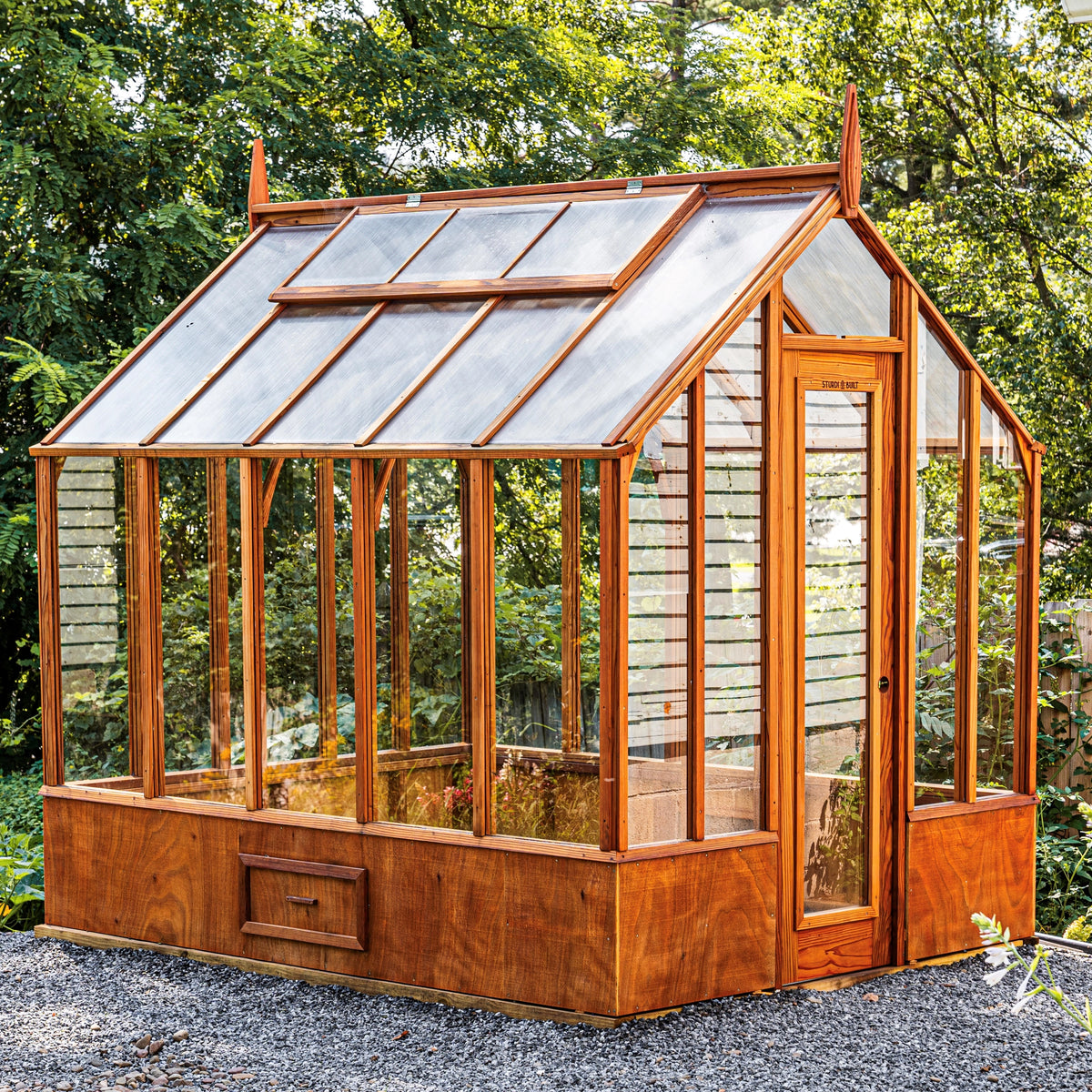 Trillium compact redwood greenhouse with tall glass walls, built-in base wall, and small garden footprint