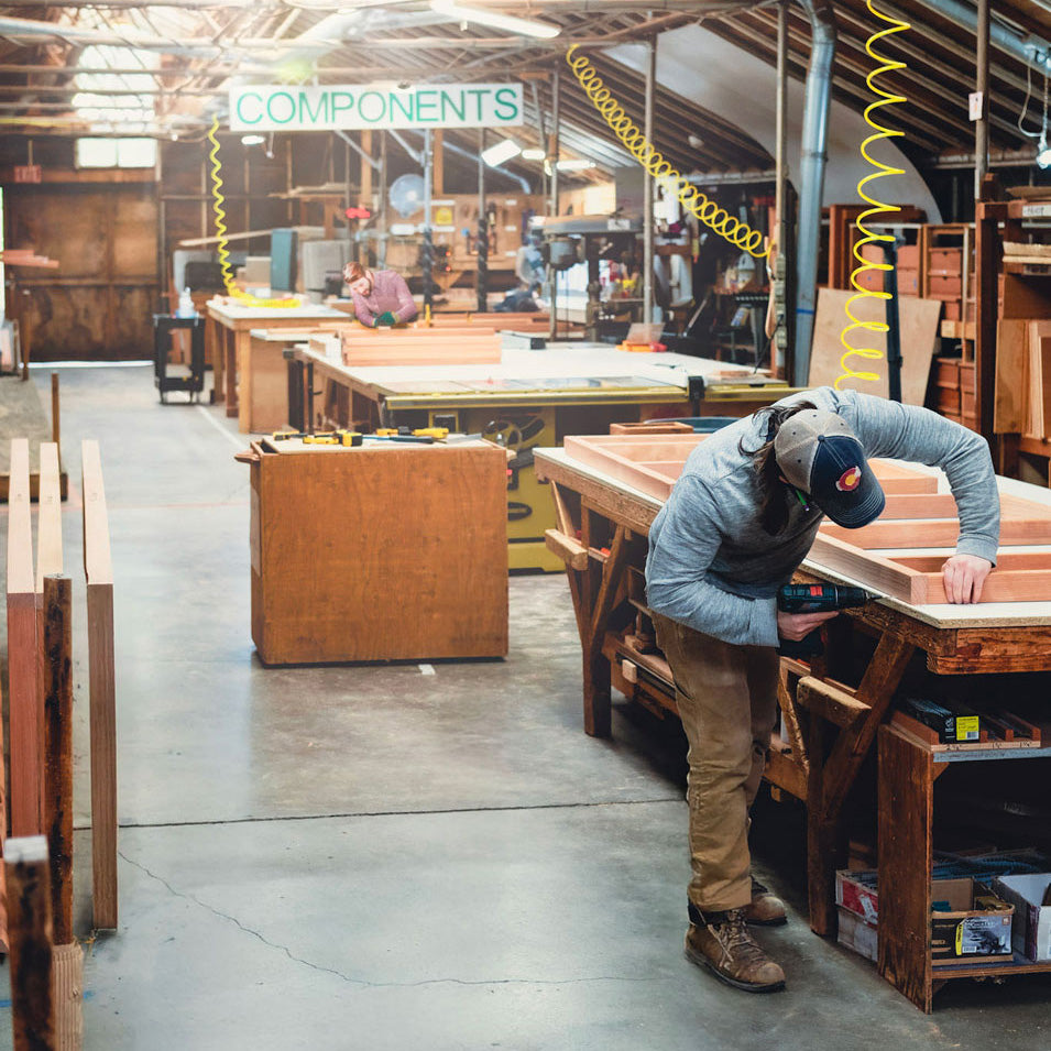 Person working on a wooden project in a workshop with 'COMPONENTS' sign in the background.