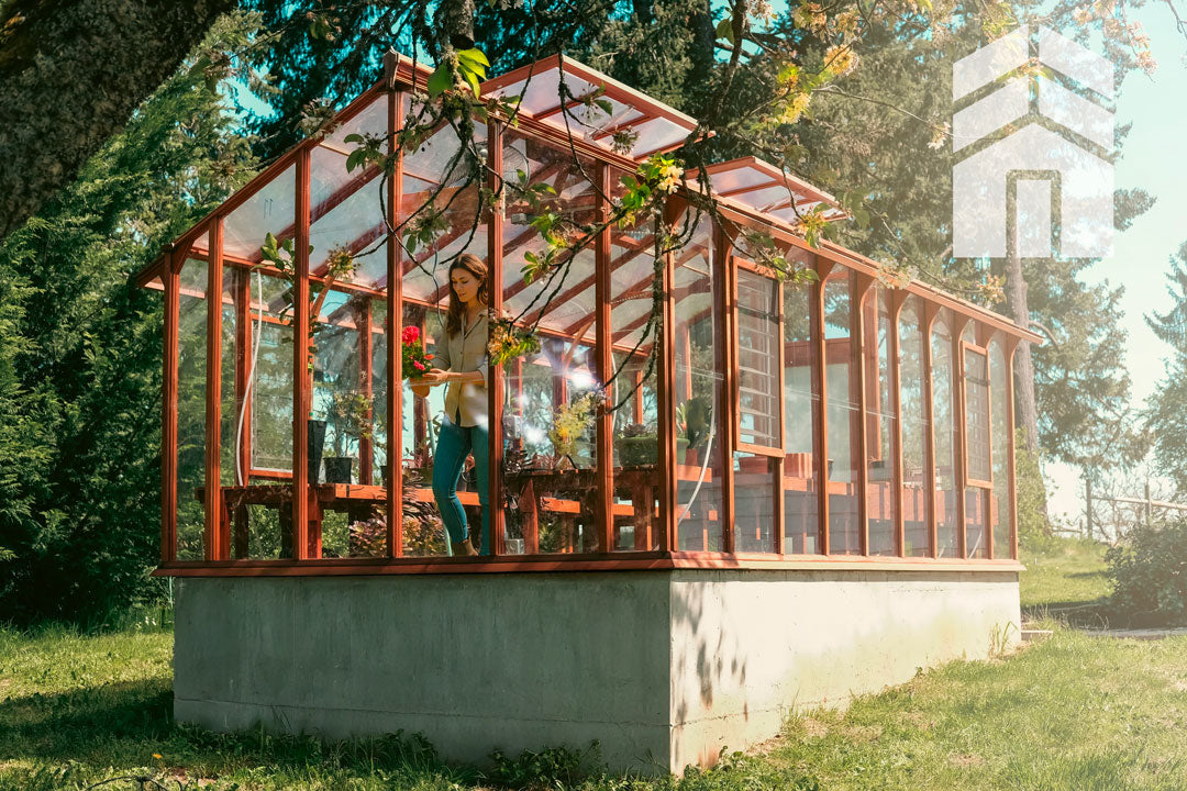 Glass greenhouse with a person inside, surrounded by trees and greenery