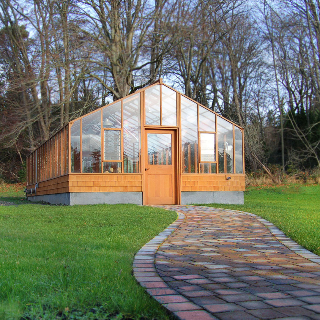 Modern Heirloom greenhouse with wooden exterior and glass panels, surrounded by trees and a grassy area.