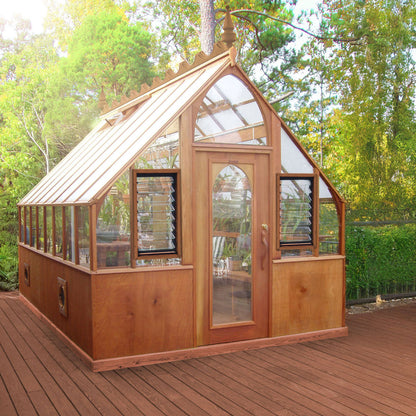 Wooden greenhouse with glass panels on a wooden deck surrounded by trees