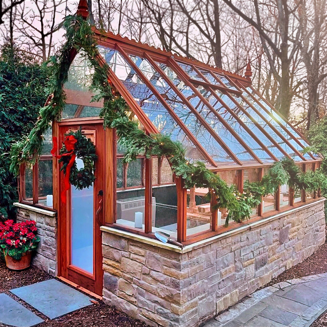 Greenhouse decorated with Christmas garlands and wreaths, surrounded by trees and potted plants.