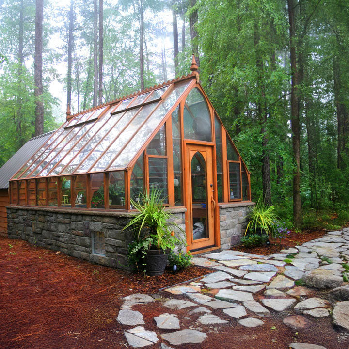 Glasshouse with stone foundation and wooden door in a forest setting