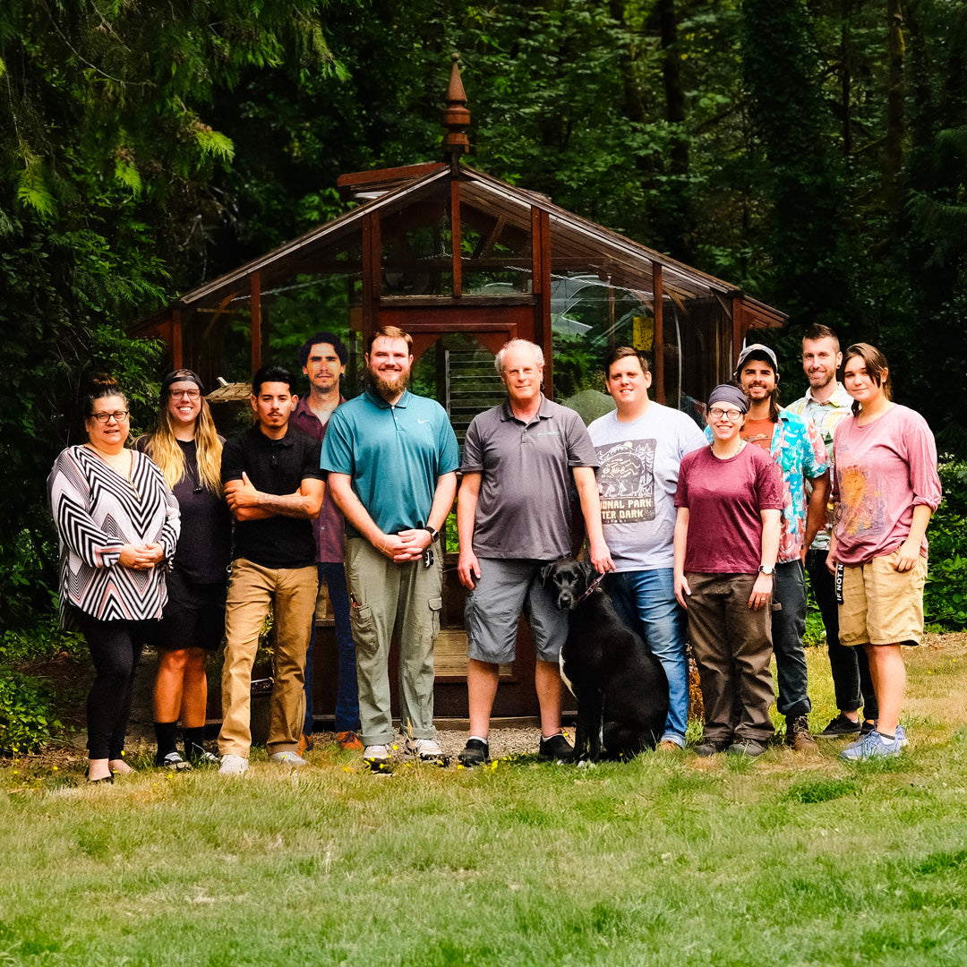 Group of people and a dog standing in front of a wooden shed with trees in the background
