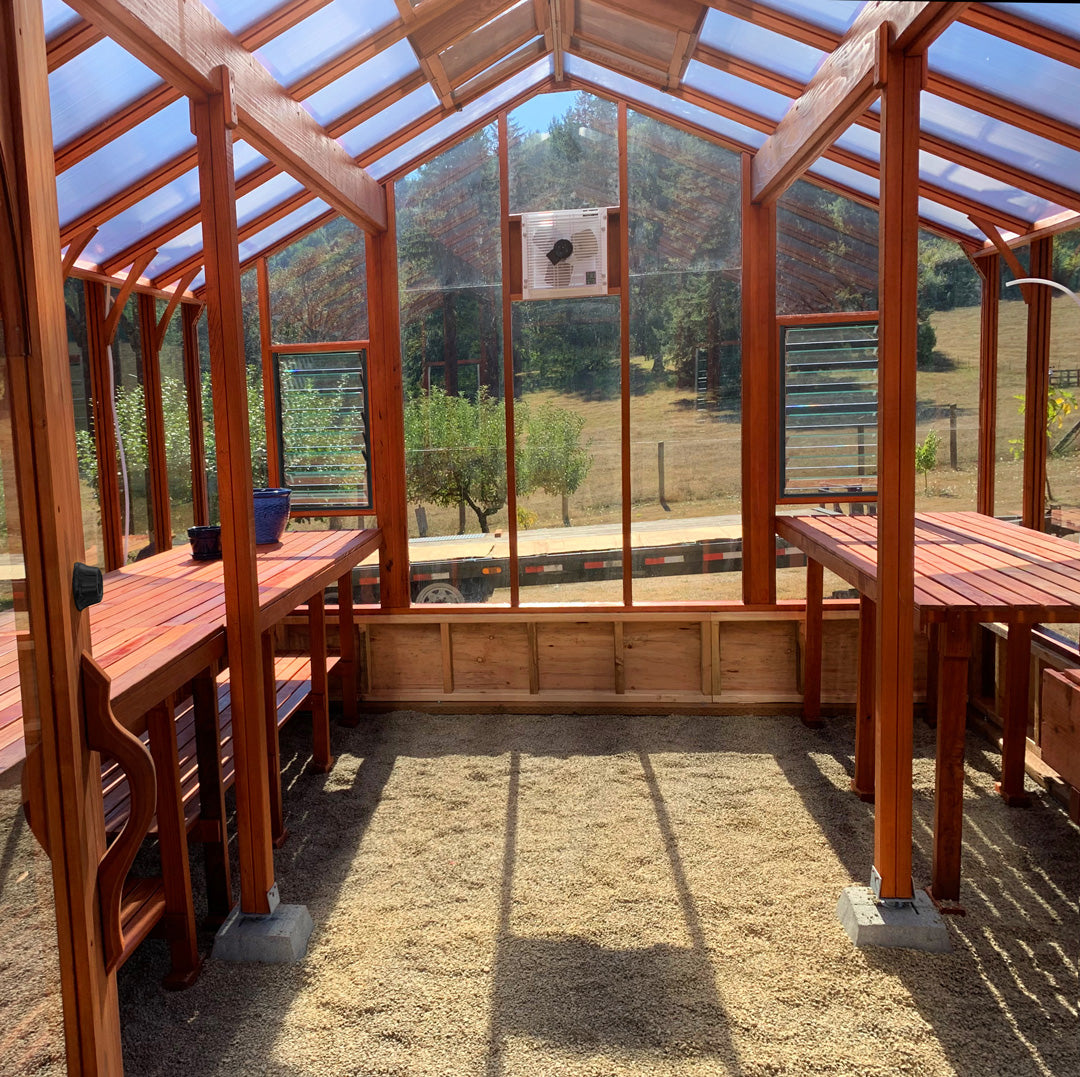 Wooden greenhouse with tables and chairs, surrounded by trees and a clear sky.