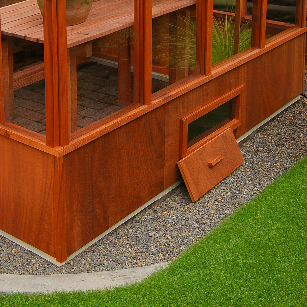 Wooden greenhouse with a base wall vent open on a grassy area